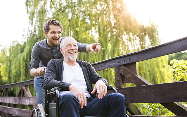 Young man pushing elderly man in a wheelchair whilst pointing