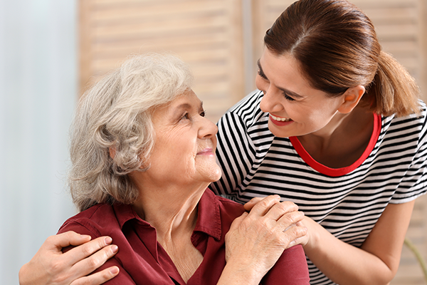 Elderly lady holding hands with care worker over her shoulder