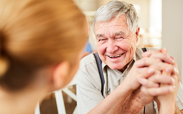 Elderly man simling and holding hands with a younger care worker