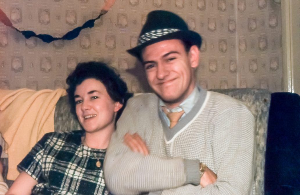 a vintage photo of a smiling young couple in their living room, which is decorated for Christmas.