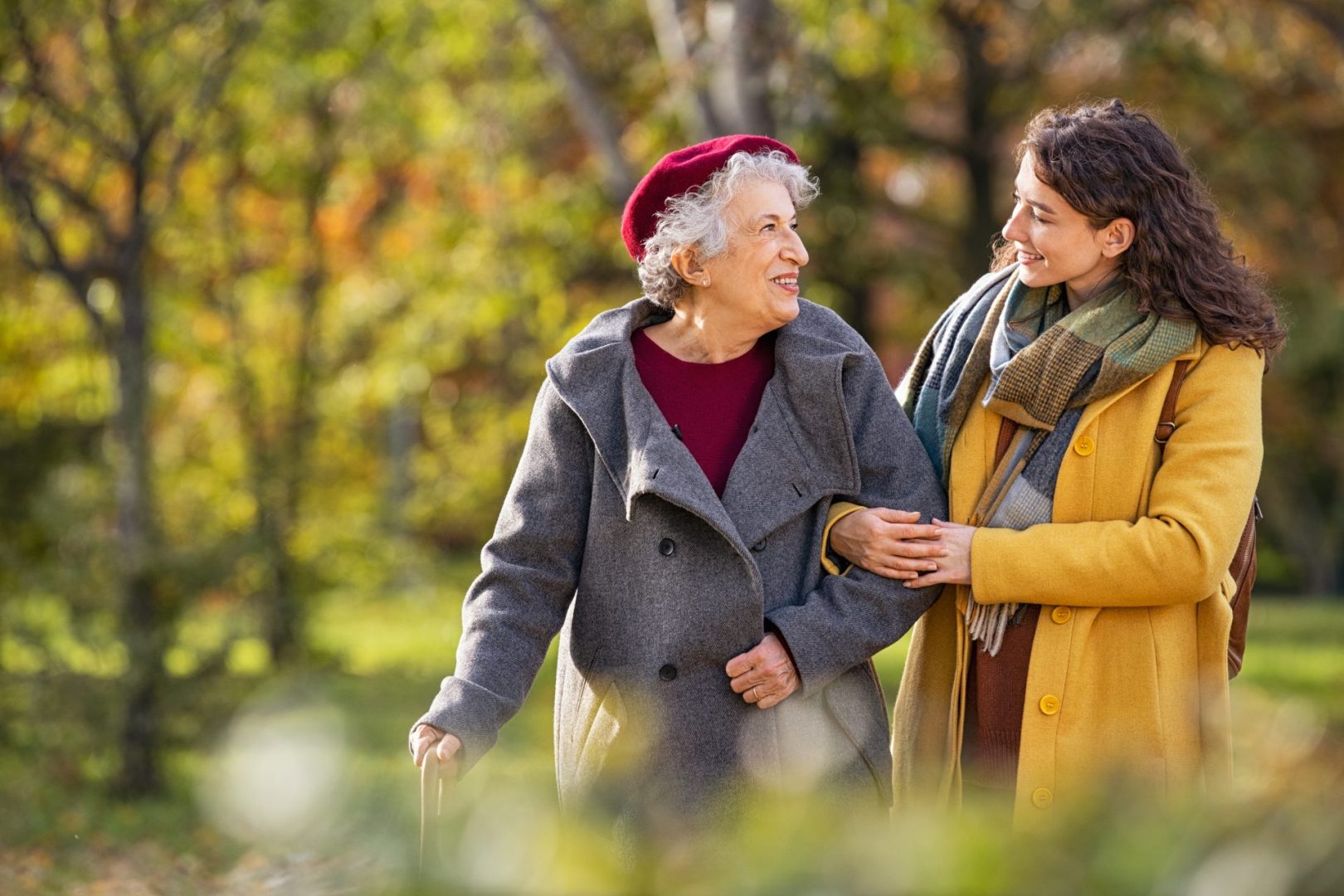 young woman taking an elderly woman for a walk in the park in winter clothing