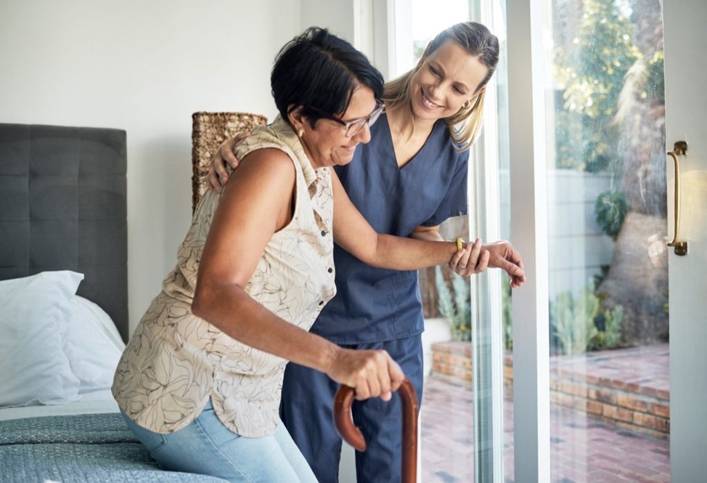 Women helping another women stand up from bed