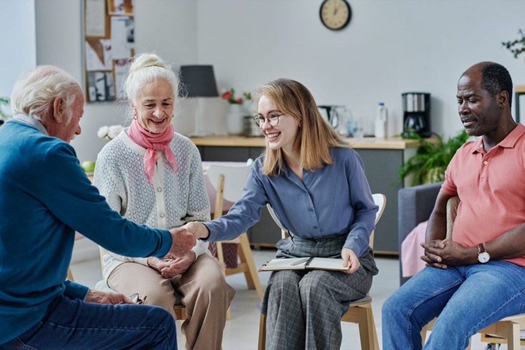 An elderly man shaking a younger woman's hand in a group setting.